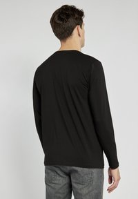 Czarna koszula z długim rękawem wykonana z miękkiej bawełny. Slim fit z okrągłym dekoltem i gładką teksturą, w zestawie z szarymi dżinsami.