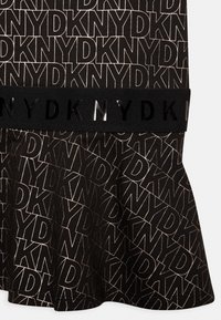 Czarna spódnica z powtarzającym się wzorem logo "DKNY" w odcieniu beżowym. Miękka tkanina z rozkloszowanym dołem oraz czarnym elastycznym pasem z błyszczącym napisem.