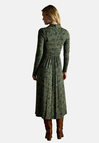 Zielona sukienka w kwiaty z długimi rękawami, dopasowanym gorsetem, marszczoną talią i zwiewnym materiałem; zestawiona z brązowymi botkami na obcasie.