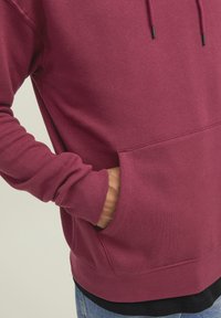 Felpa bordeaux con polsini e orlo a coste, dotata di tasca frontale a kangaroo e cordini regolabili sulla cappuccio. Tessuto in misto cotone.