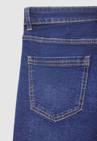 Dunkelblaue Jeans aus Denim mit sichtbarer Gesäßtasche, kontrastierenden Nähten und glatter Textur. Der Bund ist verstärkt.