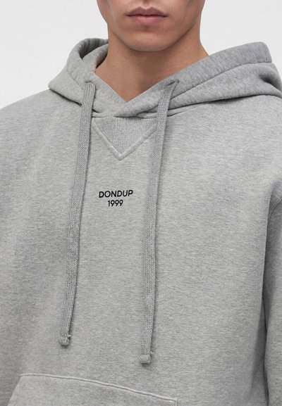 Jeune personne portant un sweat à capuche gris clair avec le texte « DONDUP 1999 » sur la poitrine et des cordons suspendus à l'avant.