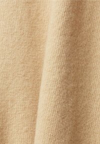 Tissu en tricot beige doux avec une texture côtelée fine et des plis subtils, suggérant chaleur et confort.