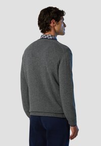 Maglione grigio a maglia con orlo e polsini a coste, indossato sopra una camicia a quadri blu. Il tessuto ha una consistenza morbida e un design classico.