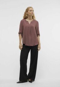 Blusa mauve a vestibilità ampia con scollatura a V e maniche arrotolate, abbinata a pantaloni neri a gamba larga e scarpe nere a punta.
