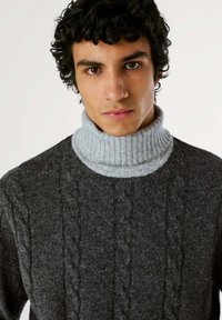 Maglione grigio a coste con un collo alto grigio chiaro a coste. Design aderente con un tessuto testurizzato e motivi sottili.