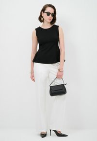Top peplum nero senza maniche, pantaloni bianchi a gamba larga, décolleté neri a punta e una piccola borsa nera. Gli accessori includono occhiali da sole e gioielli.