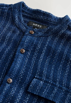 Dark blue shirt made of textured fabric with vertical white stripes. Features a stand collar and brown buttons. Includes a chest pocket.