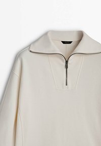 Pullover bianco sporco con collare a mezza zip, scollo a coste e maniche lunghe, esposto su uno sfondo bianco.