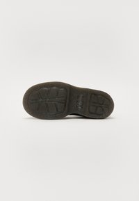 Schwarze Gummisohle mit strukturiertem Design, ausgestattet mit tiefen Rillen für besseren Halt und einer runden Form für Unterstützung.