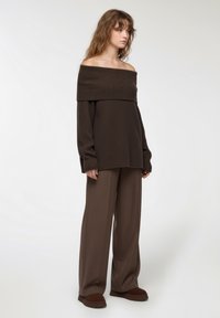 Brązowy sweter typu off-the-shoulder z prążkowanym wzorem, połączony z szerokimi spodniami w tym samym kolorze. Oba elementy mają fakturowany wzór, co tworzy spójną całość.