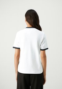 White cotton t-shirt with short sleeves, featuring a contrasting dark blue collar and sleeve edges. Back view shows a smooth, plain surface.