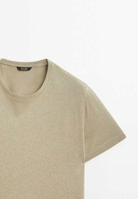 T-shirt beige à manches courtes avec col rond, posé à plat sur fond blanc, montrant le haut devant et la manche droite.