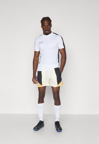 Nike sportswear sæt bestående af en hvid T-shirt med korte ærmer og sorte detaljer, lyse shorts med mesh-detaljer og sorte fodboldstøvler.