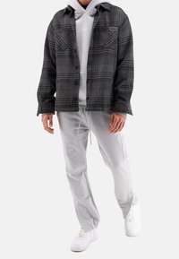 Sort og grå ternet skjortejakke med to brystlommer, båret over en lys grå hoodie og matchende sweatpants. Hvide sneakers fuldender looket.