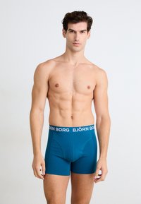 Boxer in teal realizzati in un materiale morbido, con un cinturino in vita bianco con il logo "BJÖRN BORG", caratterizzati da una vestibilità aderente e una superficie liscia.