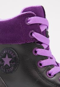 Czarny skórzany sneakers za kostkę z fioletowym zamszowym kołnierzem. Posiada fioletowe sznurówki, okrągłą naszywkę z logo oraz metalowe oczka.