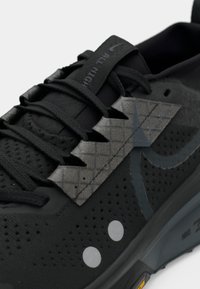 Black athletic shoe with a textured grey ankle support, intricate lacing, perforated mesh sides, and metallic accents on the sole.