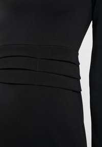 Czarna sukienka z teksturowanej tkaniny, z warstwowymi paskami w talii. Design jest dopasowany, z długimi rękawami i gładkim wykończeniem.
