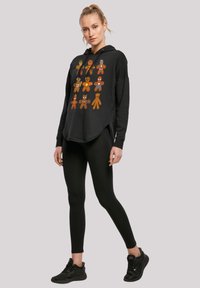 Felpa nera con stampe colorate di personaggi di pan di zenzero, vestibilità comoda, fessure laterali, abbinata a leggings neri e sneaker.