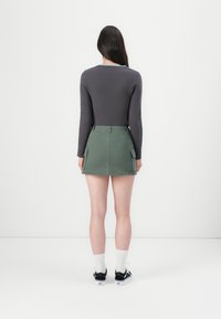 Donkergrijze longsleeve top in combinatie met een groene cargostijl minirok met twee voorzakken. Model draagt zwarte sneakers en witte sokken.