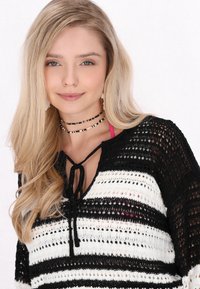Stickad tröja med svartvita horisontella ränder, med en slipsnack och ett öppet mönster. Modellen har på sig en rosa topp under.