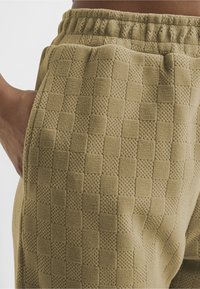 Teksturert khaki joggebukser med rutemønster, med elastisk midje og sidelommer, som fremhever et mykt, vevd materiale.