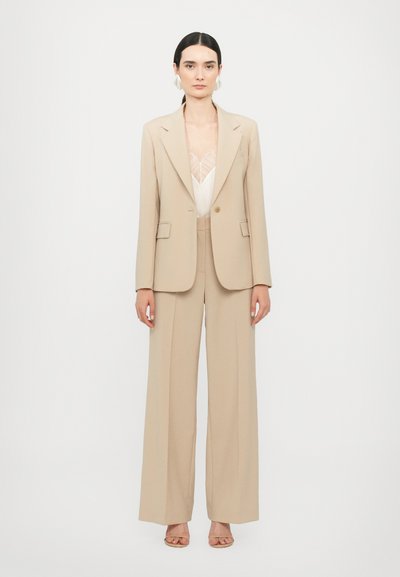 Beige op maat gemaakt pak met een blazer met één knoop en wijde broekspijpen, gecombineerd met een lichte kanten top, die een gladde textuur benadrukt.