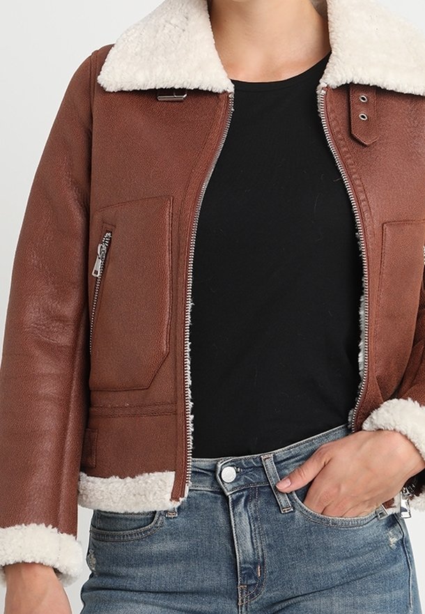 Giubbotto in pelle marrone con colletto in shearling bianco, chiusura con zip frontale e tasche laterali. Finitura testurizzata con cuciture a contrasto e polsini.