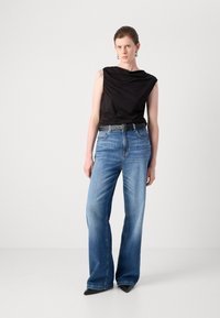 Svart ermeløs topp med drapering, blå høyt liv brede jeans, svart belte og spisse svarte hæler. Glatte teksturer.