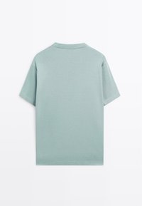 En enkel ljusblå kortärmad t-shirt sedd bakifrån mot en vit bakgrund.