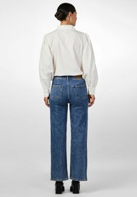 Valkoinen pitkähihainen paita, jossa on puffattuja olkapäitä, yhdistettynä korkeavyötäröisiin, leveälahkeisiin sinisiin farkkuihin. Mustat paksupohjaiset kengät.