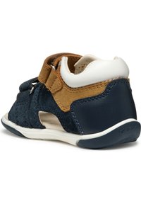 Zapato infantil de ante azul y marrón con acentos en blanco, correa de velcro, recortes para transpirabilidad y suela de goma flexible.