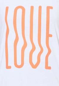 Witte T-shirt met een gestileerde "LOVE" grafiek in golvende, oranje tekst. De stof oogt zacht en lichtgewicht met een gladde textuur.