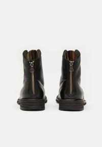 Botas negras de tobillo con un diseño perforado, cremalleras laterales y un forro a rayas multicolor en contraste. Suelas de madera planas con ligera elevación.