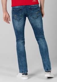 Blauwe denim jeans met een slim fit, voorzien van twee achterzakken met stikdetails, gedragen met witte sneakers en een rood shirt.