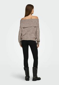 Pull en maille beige clair, décolleté sur les épaules, avec une texture côtelée. Porté avec un jean skinny noir et des bottes noires jusqu'au genou.