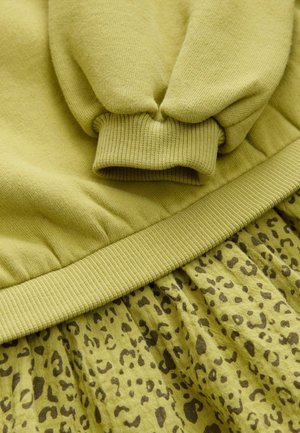Grøn bomulds sweatshirts med ribbede manchetter, parret med en matchende nederdel i leopardprint i samme farvepalette, der har en tekstureret stof.