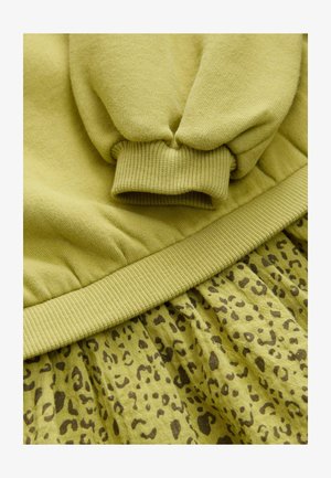 Grüner Baumwollpullover mit gerippten Bündchen, kombiniert mit einem passenden Rock im Leopardenmuster in der gleichen Farbpalette, der aus strukturiertem Stoff gefertigt ist.