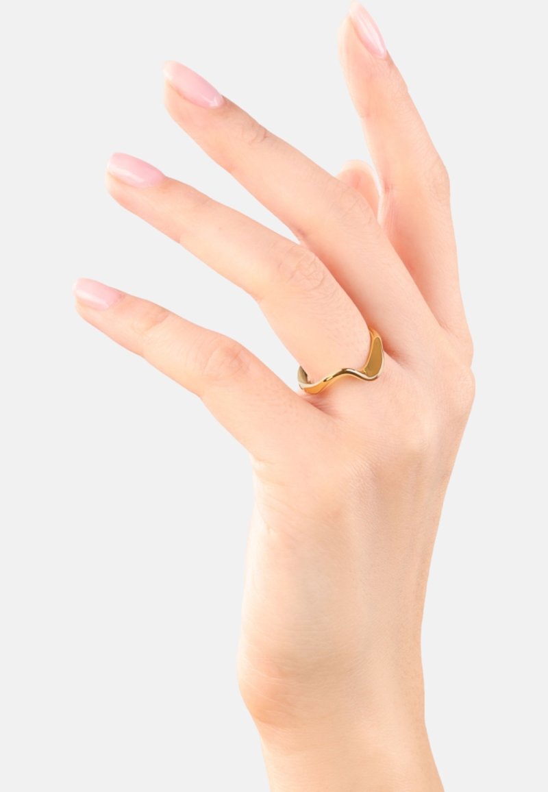 Main avec des ongles aux tons naturels portant une bague en or lisse et courbée au majeur, sur un fond clair uni.