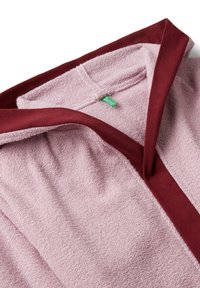 Accappatoio in spugna rosa con rifiniture in maroon, dotato di scollatura a V e superficie texture al tatto. Etichetta verde visibile all'interno.