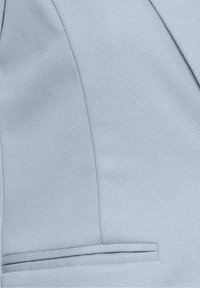 Tissu texturé bleu clair avec un gros plan sur la manche d'une veste sur mesure et le détail de la couture de la poche.