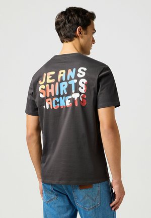 Mustat puuvillapaidat, joissa on värikkäät tekstit selkäpuolella: "JEANS SHIRTS JACKETS" punaisella, sinisellä ja valkoisella. Lyhyt hiha ja pyöreä kaula-aukko.