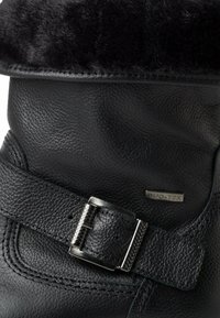 Bottine en cuir noir avec un revers en fausse fourrure, surface texturée, une boucle argentée décorative et des détails cousus, marqué "DUO-TEX".