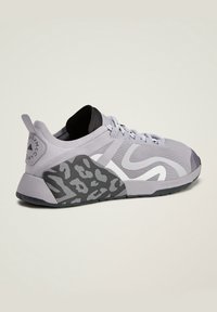 Šedá sportovní obuv s hladkým svrškem, texturovanou černo-bílou vzorovanou stélkou, plochým systémem tkaniček a značkovým detailem na patě.