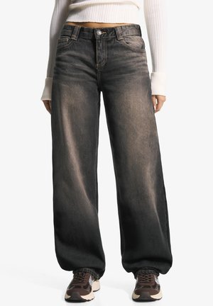 Brede zwarte denimjeans met een vervaagde afwerking, voorzien van volumineuze frontzakken, een knoopsluiting en contraststiksel. Gepaard met sneakers.