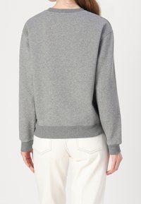 Szara bawełniana bluza z okrągłym dekoltem, ściągaczami przy mankietach i dole. Tył ma gładką fakturę i luźny krój, zestawiona z białymi spodniami.