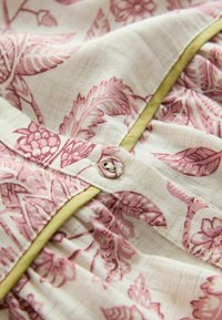 Prim-plan cu un material floral roz cu nasture mic îmbrăcat și finisaj galben pe un textile bej deschis.