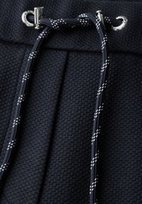 Tissu texturé bleu marine avec un motif tissé et un cordon de serrage à rayure blanche contrastante. Comprend des éléments en métal argenté au niveau de la taille.