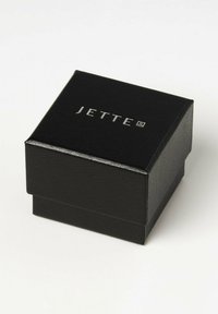 Schwarze Schmuckschatulle mit strukturierten Oberflächen, mit einem silbernen "JETTE"-Logo, das auf dem Deckel eingeprägt ist; quadratische Form mit Klappdeckel.